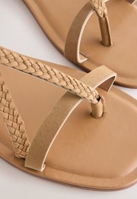 Tanfarvede sandaler med flettet remdesign, flad sål og glat tekstur. Fremstillet med fleksible materialer for komfort.