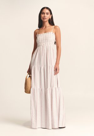 Maxi šaty v bílé barvě s červenými vertikálními pruhy. Mají nastavitelné ramínka a nařasený živůtek, s volánovou sukní.