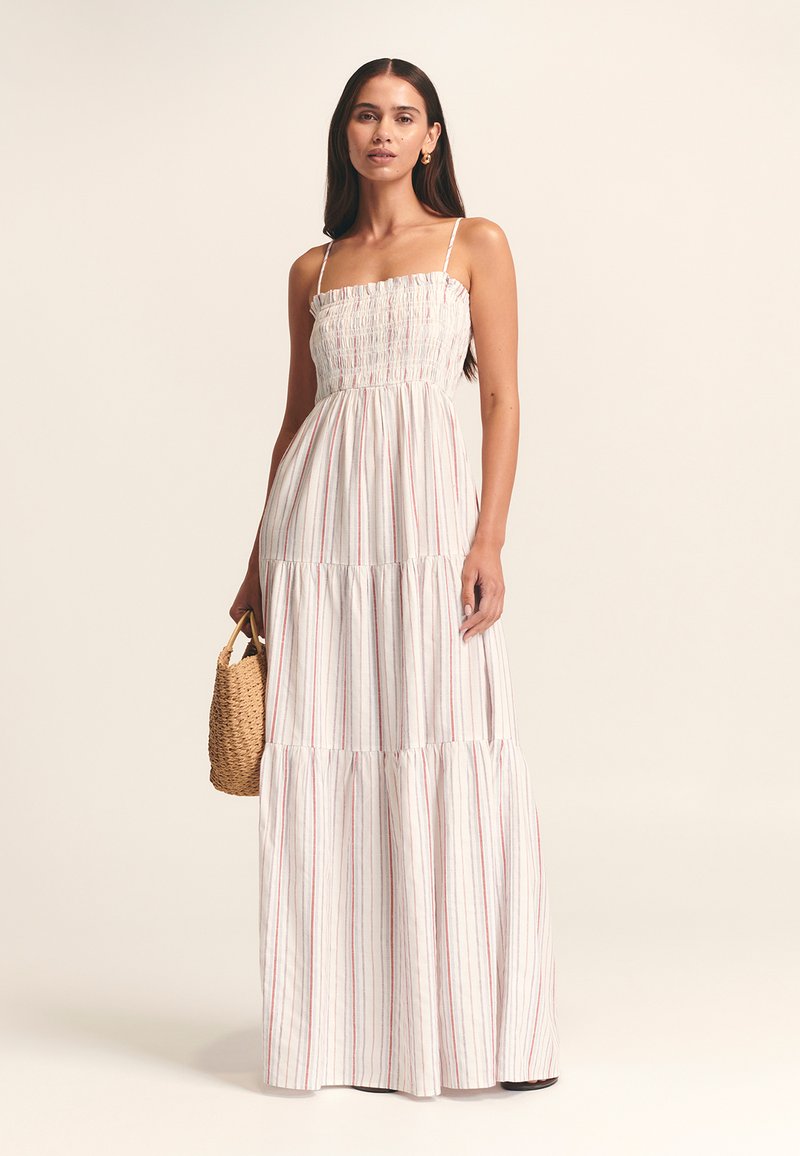 Vestido maxi con corsé fruncido, tela blanca con rayas verticales rojas, tirantes finos, diseño de capas y un bolso tejido con textura.