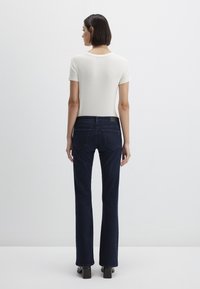 Dark blue flared jeans with a smooth texture, high waist, and four pockets. Paired with a fitted, light-colored short-sleeve top.
