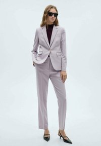 Costum lila la comandă, cu o jachetă ajustată și pantaloni drepti, asortat cu un top burgundy și pantofi cu vârf ascuțit negri.