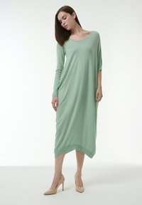 Vestido de manga larga en verde menta con escote redondeado y dobladillo desigual. Tejido suave que cae con suavidad; combinado con tacones nude.