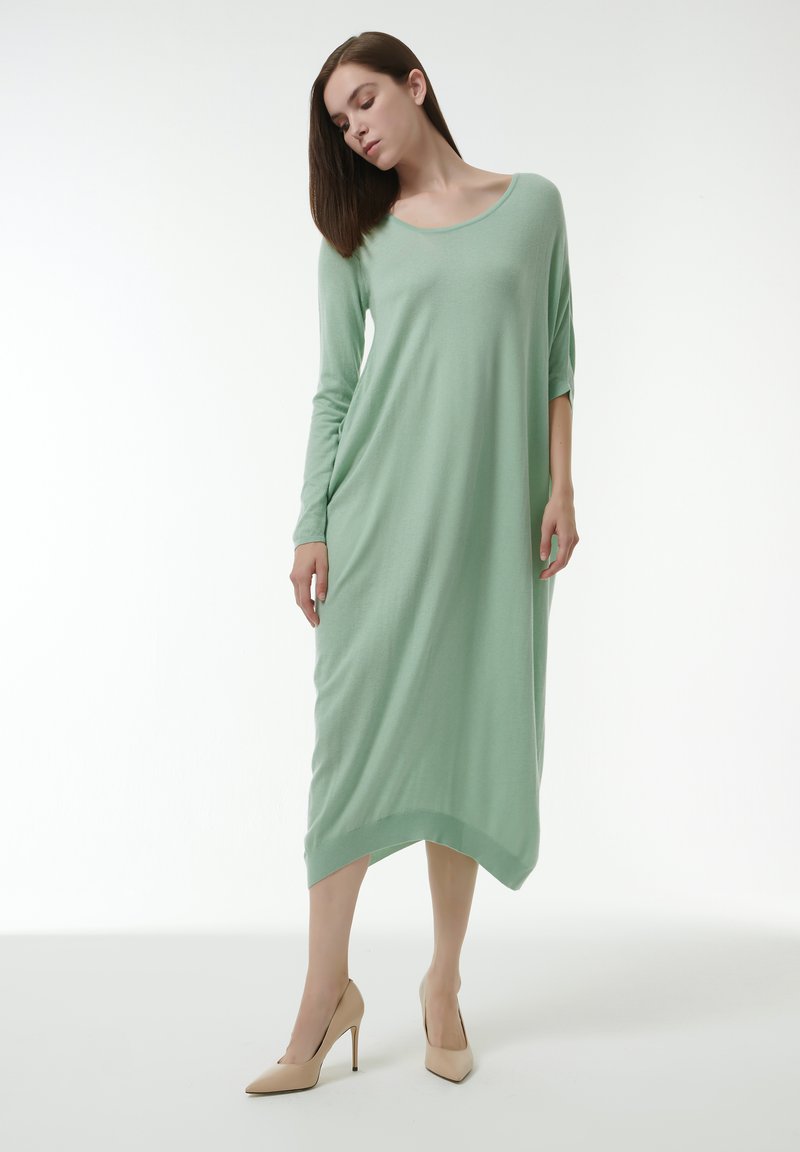 Vestido de manga larga en verde menta con escote redondeado y dobladillo desigual. Tejido suave que cae con suavidad; combinado con tacones nude.