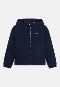 Navy blue hooded jacket with a front zipper, textured material, elastic cuffs, and a small green embroidered logo on the chest.