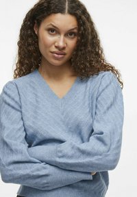 Hellblau gestrickter Pullover mit V-Ausschnitt, der eine dezente Zickzackstruktur aufweist, lange Ärmel sowie gerippte Bündchen und Saum hat.