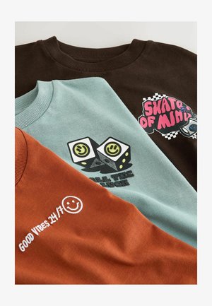 Drie crewneck sweatshirts: bruin met grafische tekst, teal met ontwerpen van dobbelstenen, en roestkleurig met witte geborduurde tekst en een glimlachend gezicht.