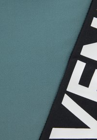 Čierna látka s veľkým bielym textom na textúrovanom teal pozadí. Zameranie na kontrast medzi farbami a vzormi.