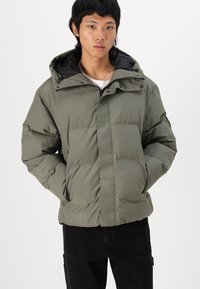 Olive green puffer jacket with a hood, featuring a zip front, side pockets, and a textured finish. Black lining and accents included.