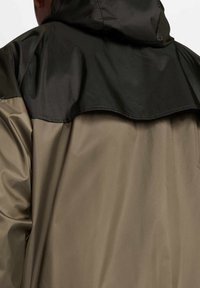 Lekka, długorękawowa kurtka w kolorze khaki i czarnym. Posiada gładką, błyszczącą górną warstwę oraz miękką, matową dolną część z kapturem.