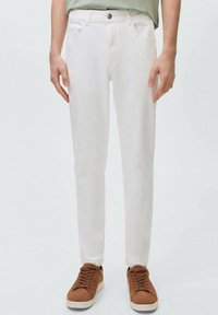 Jeans de mezclilla blanca con corte recto, que cuentan con bolsillos delanteros, un cierre de botón y detalles de costura sutiles. Se llevan zapatillas de ante marrón.