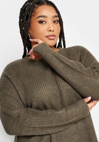 Olivgrüner gestrickter Pullover mit geripptem Muster, Rundhalsausschnitt und langen Ärmeln. Verfügt über eine oversized Passform mit verlängerten Ärmelbündchen.