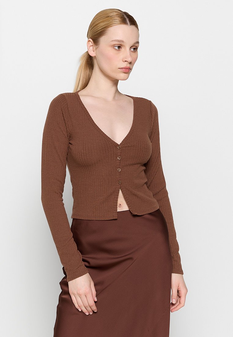 Brauner gerippter Longsleeve-Cardigan mit V-Ausschnitt, ausgestattet mit fünf Knöpfen auf der Vorderseite, kombiniert mit einem passenden braunen Rock.