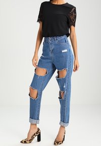 Sort top med blonderærmer, høj talje blå ripped jeans og leopardmønstrede blokhælede sko. Har frynsede kanter og oprullede manchetter.