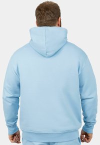 Felpa azzurra chiara con una texture morbida, dotata di un ampio cappuccio, maniche lunghe e polsini e orlo a coste. La vista posteriore mostra un design liscio e senza cuciture.