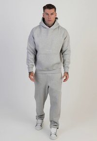 Szara bawełniana bluza z kapturem, kieszenią kangurką i ściągaczami na rękawach, w zestawie z pasującymi dresami. Oba elementy mają subtelne białe logo.