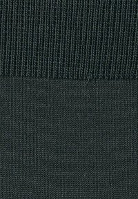 Dunkelgrüner Stoff mit einer gestrickten Textur. Verfügt über einen gerippten oberen Rand und eine glatte, gleichmäßige Oberfläche darunter.