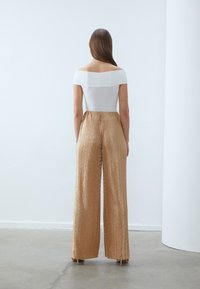 Haut blanc à épaules dénudées associé à un pantalon large plissé doré, avec une finition texturée et une taille haute.