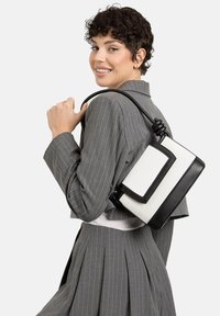 Borsa nera e bianca con design rettangolare, caratterizzata da un corpo in tessuto testurizzato, dettagli in pelle liscia e una tracolla annodata.