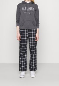 Grå huvtröja med en vit logotyp, tillsammans med svart och vit rutiga vida byxor. Vita sneakers fulländar den avslappnade stilen.