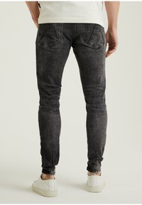 Jeans negros ajustados con una textura desgastada, con bolsillos de parche y un ajuste elegante, combinados con zapatillas blancas.