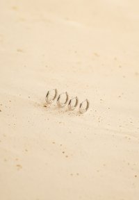 Cztery srebrne kolczyki w kształcie kół o różnych rozmiarach, charakteryzujące się gładką, wypolerowaną powierzchnią o subtelnym blasku, wyeksponowane na neutralnym, piaskowym tle.