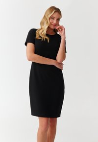 Robe noire à manches courtes avec une silhouette ajustée, dotée d'un design texturé et d'un col rond. Tissu lisse avec un minimum de détails.
