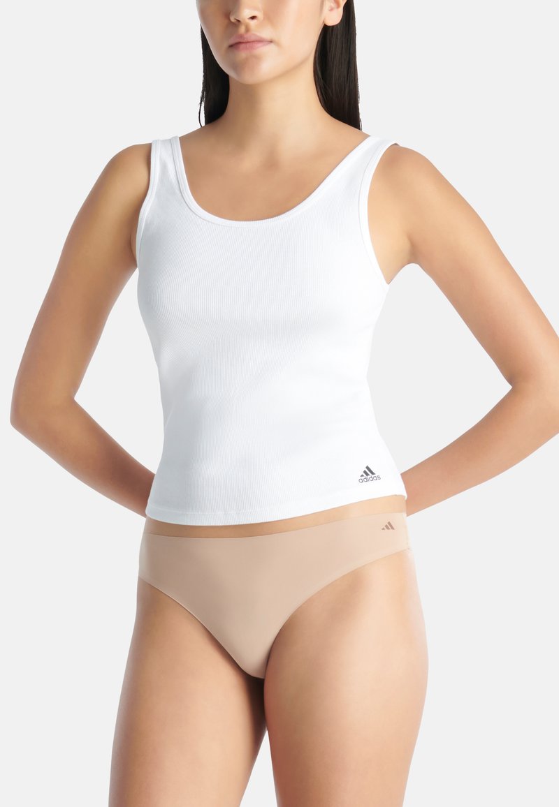 Witte geribbelde tanktop met brede schouderbanden en lichtbeige naadloze ondergoed, voorzien van zwarte logo-accenten op beide items.