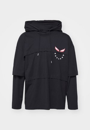 Sudadera negra con capas y cuello alto, que presenta un bolsillo frontal, gráficos de alas rojas en contraste y un patrón de estrellas en el lado izquierdo.