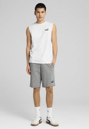 Witte mouwloze shirt met zwart Puma-logo, gecombineerd met grijze shorts met logo, gedragen met witte sokken en sneakers met zwarte accenten.