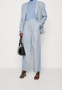 Lichtblauwe gestreepte blazer en broek, gecombineerd met een bijpassende coltruibodysuit. Een zwarte handtas en sandalen met open tenen maken de look compleet.