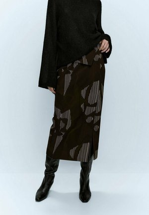 Długa brązowa spódnica z geometrycznym wzorem w ciemniejszych odcieniach oraz cienkimi białymi paskami. Połączona z czarnym swetrem o fakturze i wysokimi kozakiem za kolano.
