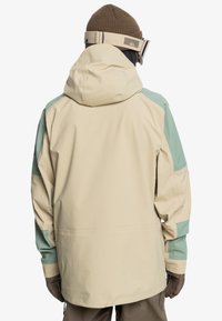 Giubbotto impermeabile beige e verde menta con cappuccio, caratterizzato da una vestibilità rilassata, polsini elasticizzati e orlo regolabile. Tessuto testurizzato.