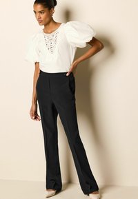 Valge puff-sleeve blouse pitsdetailidega, mis on ühendatud mustade kohandatud pükste jahedas kombinatsioonis. Rõivakomplektil on sobiv talje ja küljetaskud.