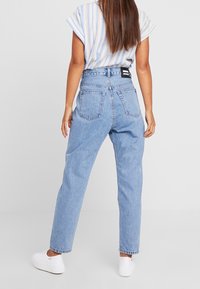 Světle modré džíny s vysokým pasem a volným střihem, se dvěma zadními kapsami a značkovým černým štítkem na pase.