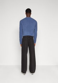 Blå genser med rund hals, parret med løstsittende sorte jeans, sett bakfra. Genseren har en teksturert overflate.