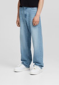 Ljusblå denimjeans med en avslappnad passform, med en klassisk femficksdesign och sömdetaljering, tillsammans med vita sneakers.