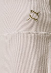 Světlé béžové žebrované látky s zlatě vyšitým logem, s čistým šitím a hladkým povrchem. Jednoduchý design bez vzorů.