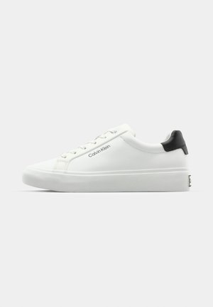 Baldos suknelės sportbačiai su lygiu paviršiumi, juodu kulno akcentu ir raištelių dizainu. Šone matoma "Calvin Klein" prekės ženklo ženklas. Minimalistinio stiliaus.