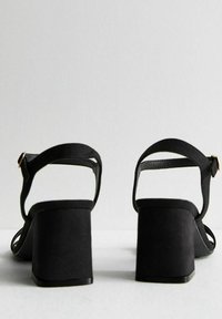Svarta blockklack-sandaler med mocka-yta, med öppen bak, tunna ankelband och en minimalistisk design.