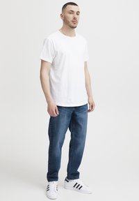 Hvit bomulls-t-skjorte med rund hals, kombinert med blå denimjeans. Fottøy inkluderer hvite joggesko med svarte striper.