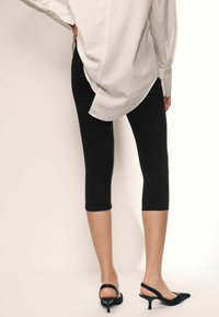 Leggings neri al ginocchio realizzati in tessuto elasticizzato, abbinati a décolleté neri con punta affusolata e tacco sottile.