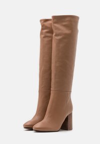 Kniehohe, hellbraune Lederstiefel mit glatter Textur, quadratischer Zehenform und einem klobigen Holzblockabsatz. Keine sichtbaren Verschlüsse oder Verzierungen.