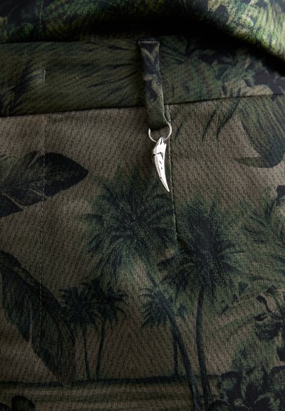 Green patterned fabric featuring palm leaves, with a silver accent on the waistband. Texture appears textured and slightly woven.