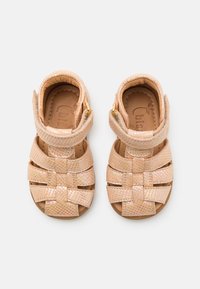 Sandali per bambini di colore rosa chiaro con una chiusura a crisscross, dotati di una piccola fibbia dorata, mostrati da una vista dall'alto.