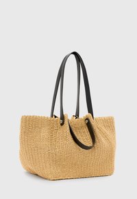 Borsa tote in paglia intrecciata beige con due manici in pelle nera, caratterizzata da un design strutturato e una parte superiore arricciata.