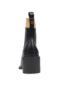 Botín de cuero negro hasta el tobillo con un detalle de corcho texturizado en la parte superior, tacón rectangular y una tira en la parte trasera para facilitar su puesta.