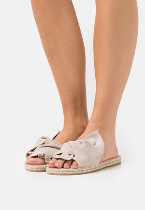 Light beige slip-on sandals with a knotted fabric upper, jute-wrapped sole, and open-toe design. Smooth texture and minimalist style.