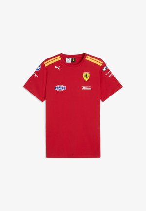 Czerwona koszulka Puma z krótkim rękawem, żółtymi paskami na ramionach, logo Ferrari oraz wieloma logo sponsorów na piersi i rękawach.