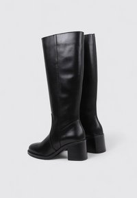 Botas de cuero negras hasta la rodilla con un tacón bloque grueso, que presentan una textura suave y costuras mínimas para un diseño elegante.