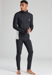 Zwarte trainingstop met lange mouwen en ritskraag, witte zijpanelen en logo. Gecombineerd met strakke zwarte leggings. Glad, rekbaar materiaal.